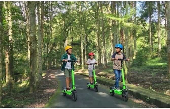 Three kids riding electric scooters through a lush forest path in Bali highlands